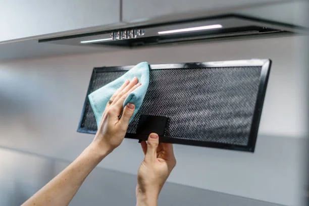 Home 16 A person cleans a kitchen range hood filter using a blue cloth.